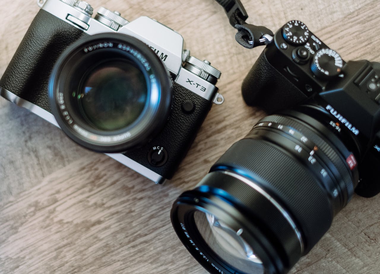 Close-up of two mirrorless cameras with lenses on a wooden background, showcasing vintage style and design.