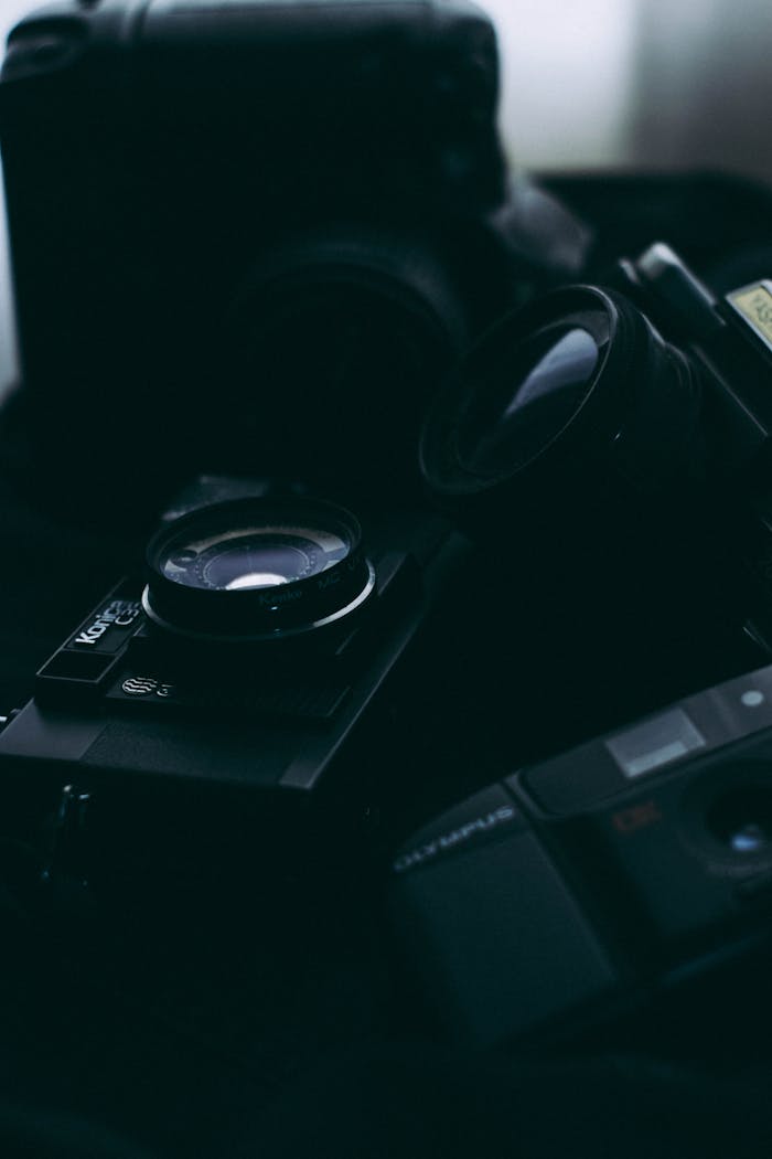 A dark, close-up image of vintage and modern camera equipment with lenses.