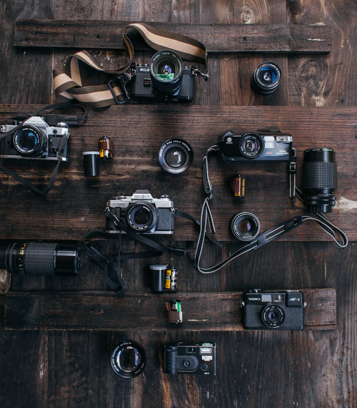 A top view of assorted vintage cameras and lenses arranged on a rustic wooden surface.